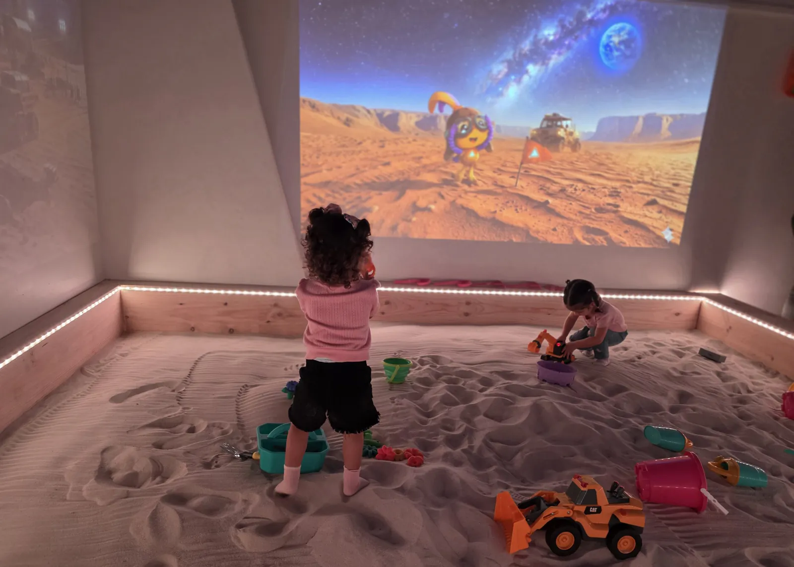 Niños y niñas en el sandbox frente a un paisaje proyectado